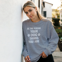 Load image into Gallery viewer, Graphite Heather - Be The Person Your Dog Thinks You Are sweatshirt, worn by a woman leaning on a white wall
