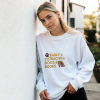 Load image into Gallery viewer, White - Easily Distracted by Dogs and Books sweatshirt, worn by a woman leaning on a white wall
